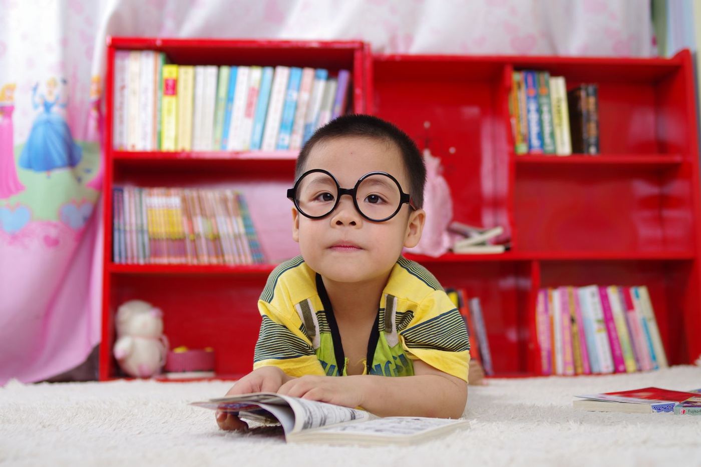 A young boy in round glasses reading in front of a bookshelf