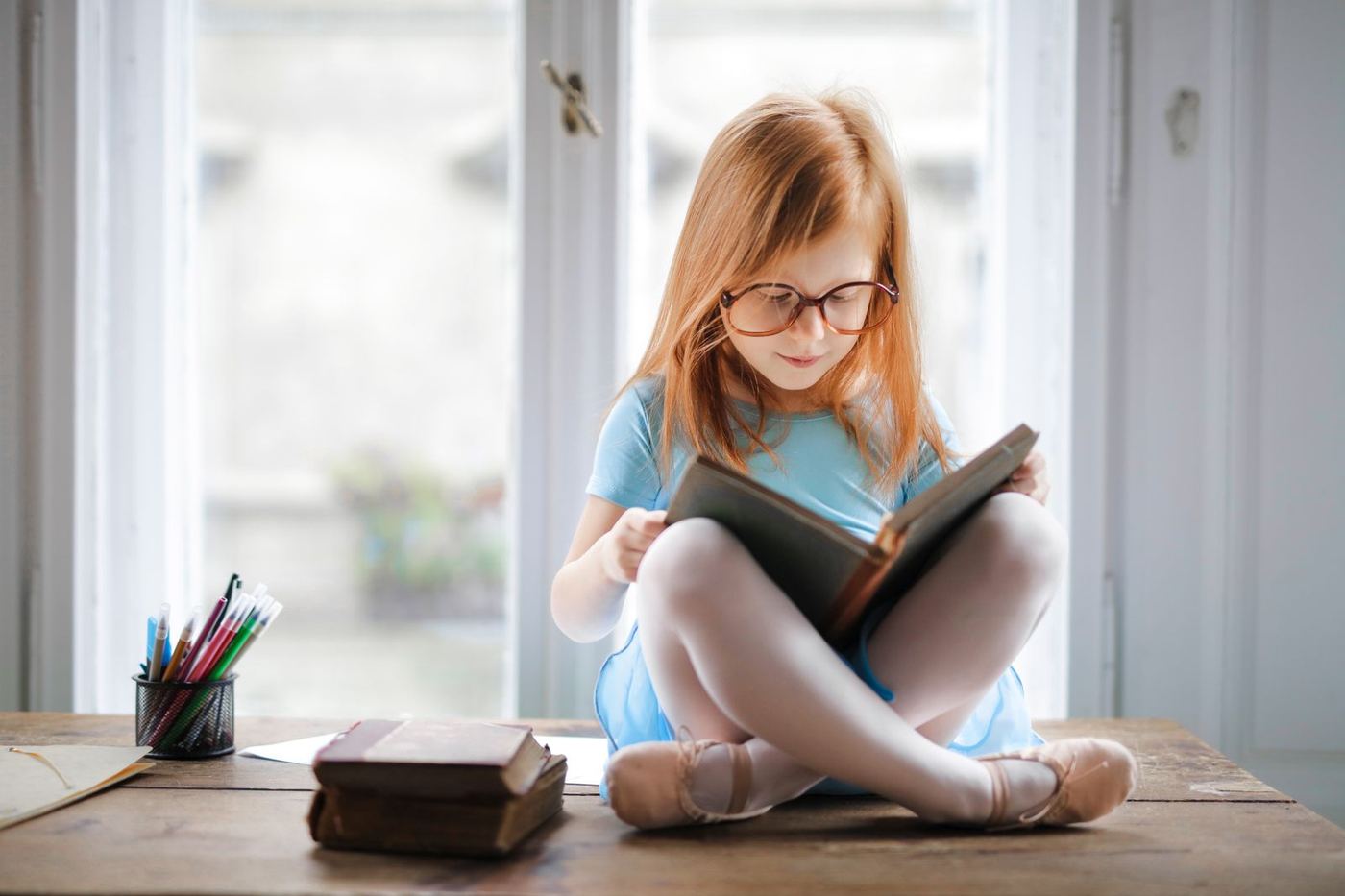 A girl wearing glasses reading a book by a window